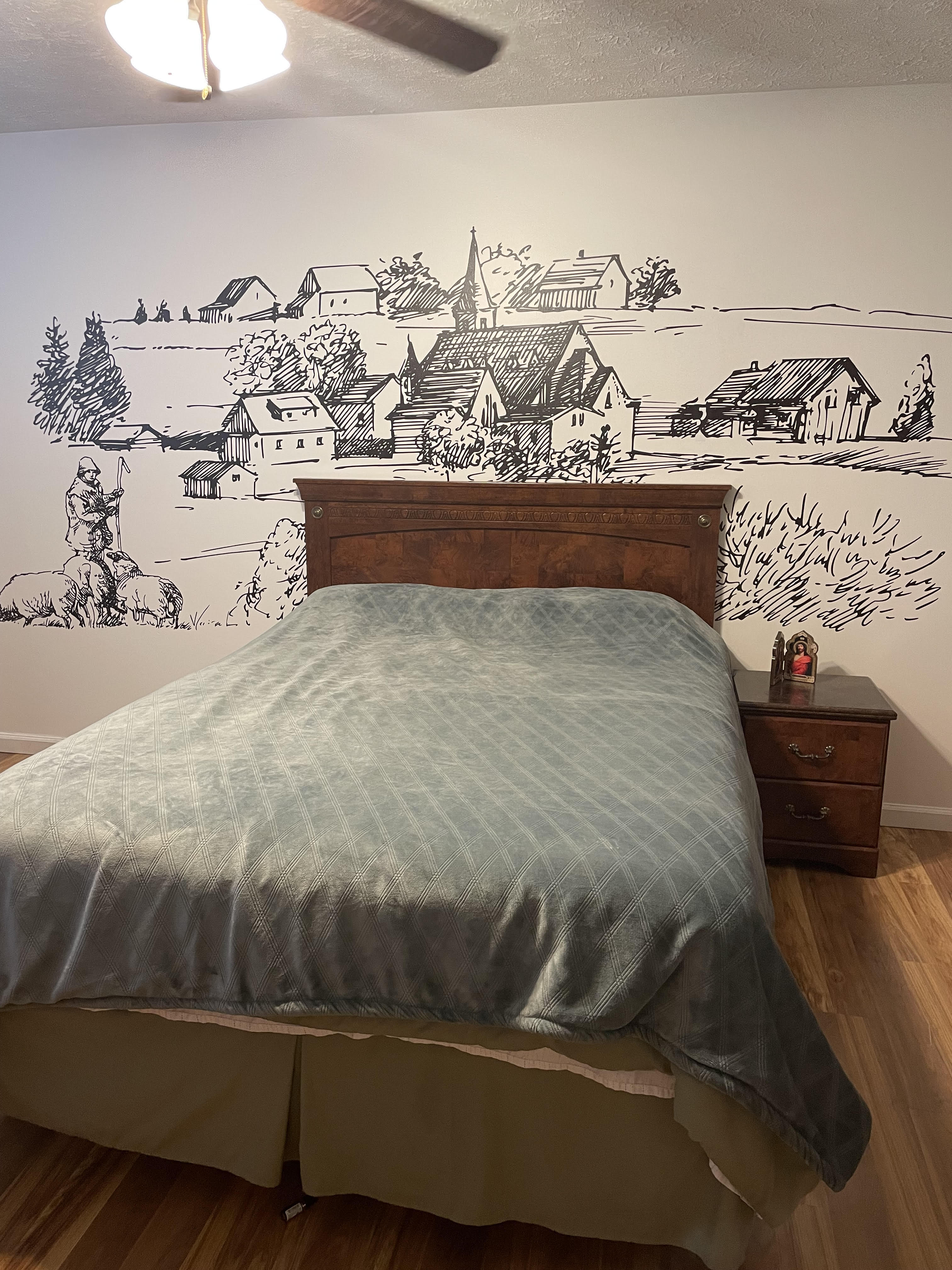 Single-color European village mural above a wooden bed headboard